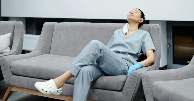 Female nurse resting on a sofa with her face towards the ceiling, and her eyes shut. Photo: Cedric Fauntleroy, from Pexels.